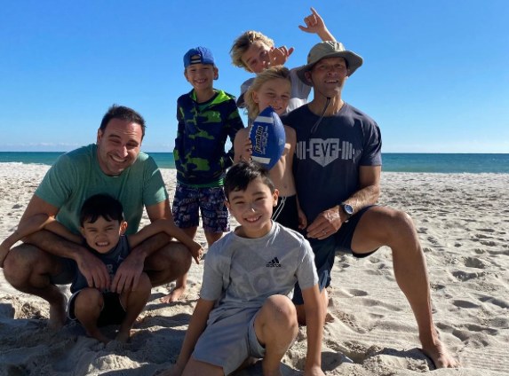 Eric and a friend on the beach with a group of smiling boys, one holding a football