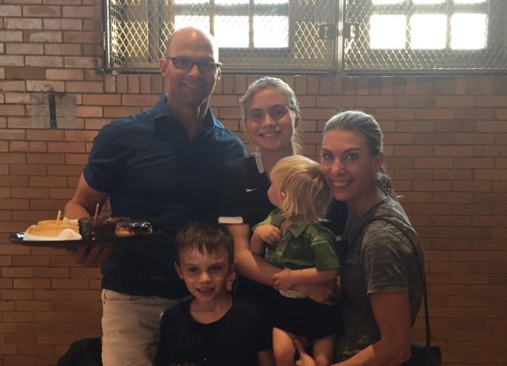 Eric holding a birthday cake with family gathered against a brick wall
