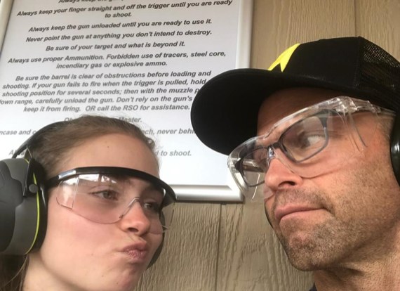 Eric and a young woman in safety glasses and ear protection making faces at a shooting range